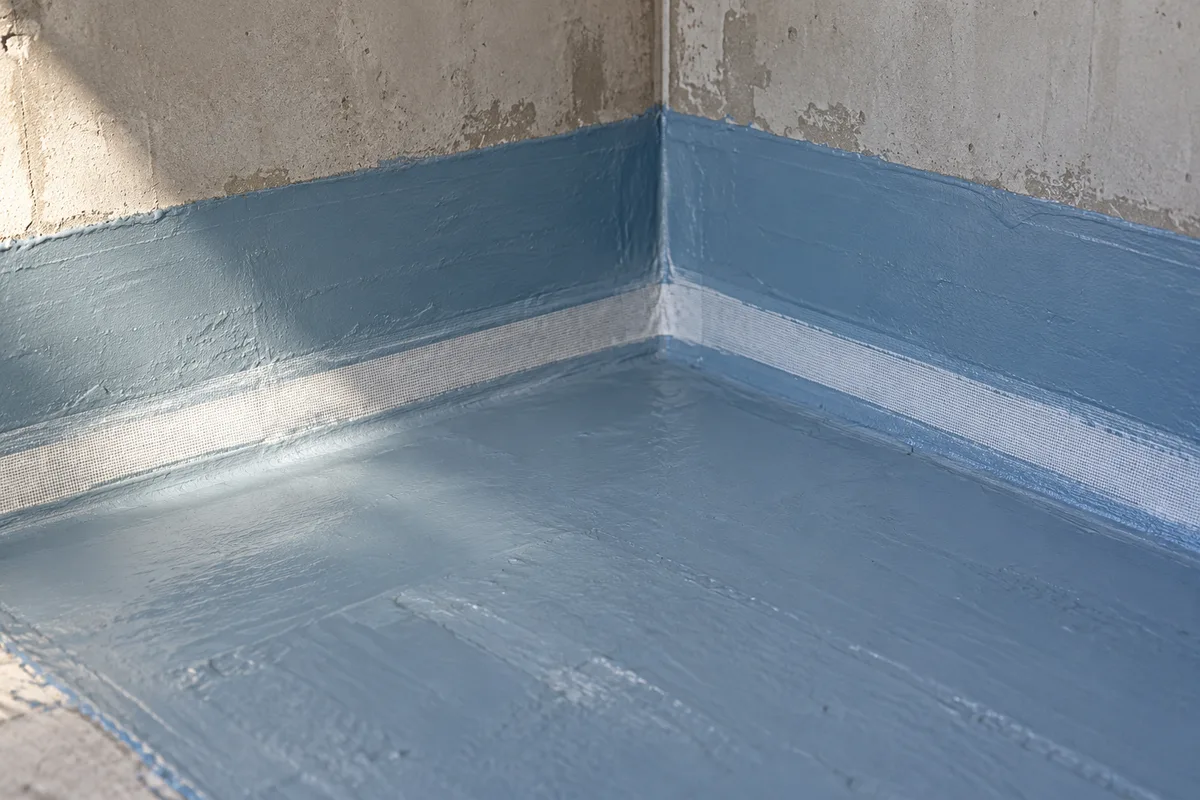 Membrane d&rsquo;étanchéité bleu-gris remontée en pied de mur dans l&rsquo;angle d&rsquo;une douche en chantier