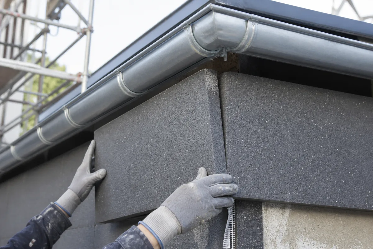 Détail de la jonction entre panneaux isolants gris et bas de toiture sur un chantier de rénovation en Île-de-France